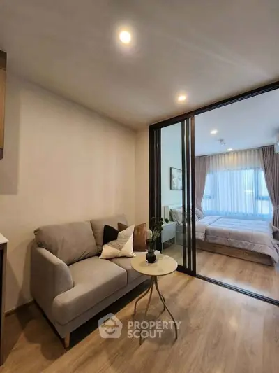 Modern apartment with cozy living room and stylish bedroom separated by glass sliding doors.