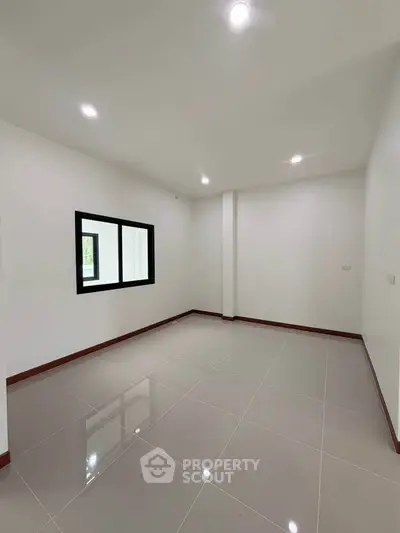 Spacious empty room with glossy tiled floor and large window, perfect for customization.