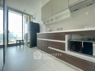 Modern kitchen with sleek cabinetry, large windows, and city view, featuring appliances like fridge and microwave.
