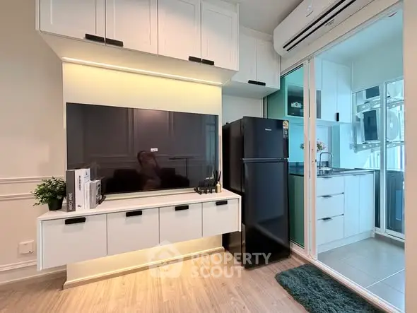 Modern living room with sleek TV setup and compact kitchen area, featuring stylish cabinetry and appliances.