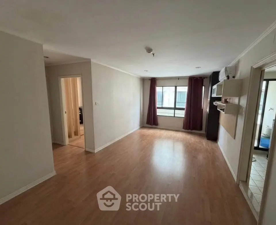 Spacious empty living room with wooden flooring and large window in modern apartment.