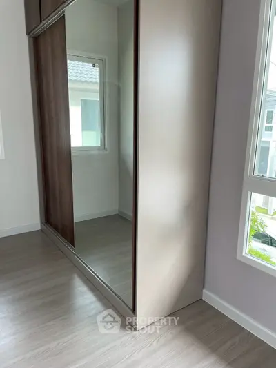 Modern bedroom with sleek mirrored wardrobe and large windows for natural light.