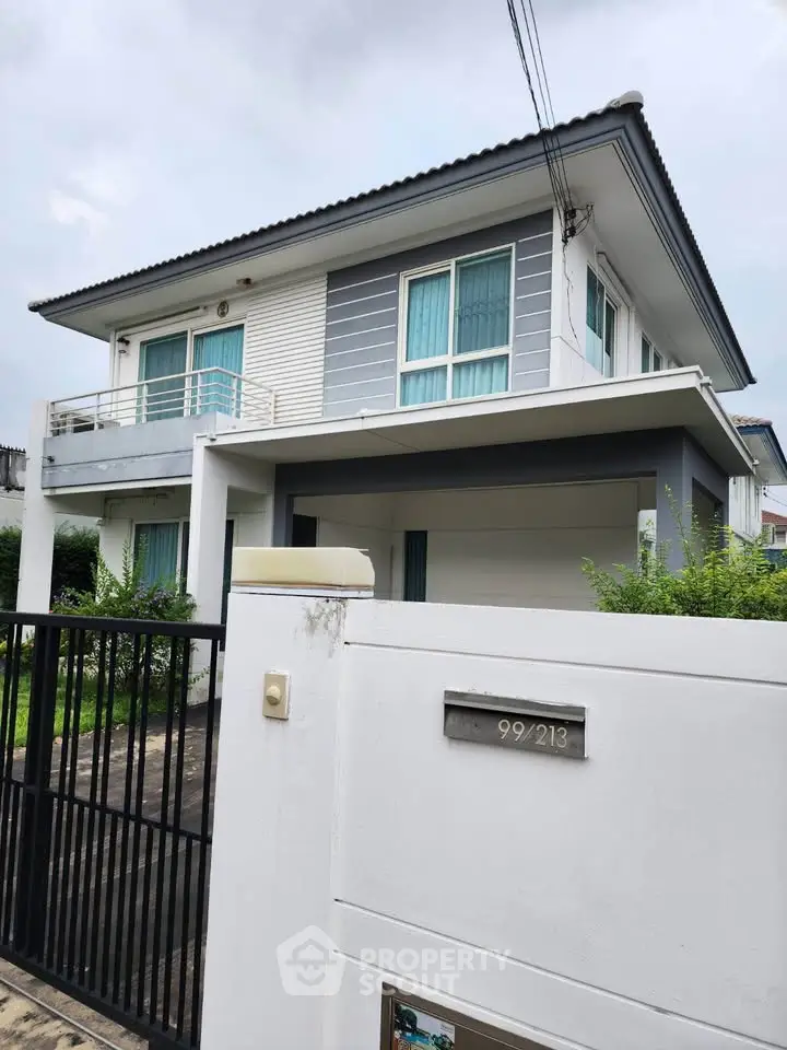 Modern two-story house with balcony and gated entrance, featuring sleek design and large windows.