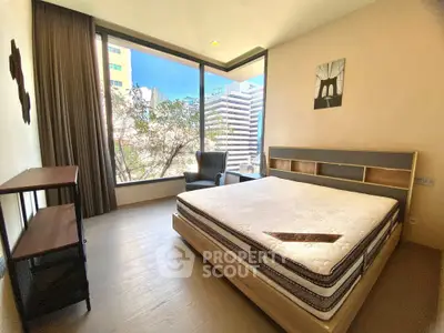 Spacious bedroom with large windows offering city views, featuring a modern bed and cozy seating area.