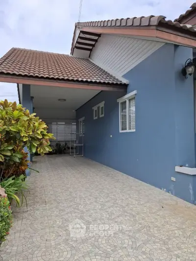 Charming blue house exterior with tiled driveway and lush greenery