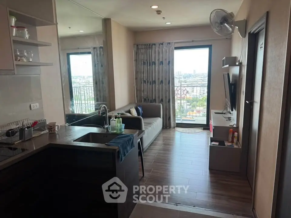 Modern living room with open kitchen and city view from balcony in high-rise apartment.