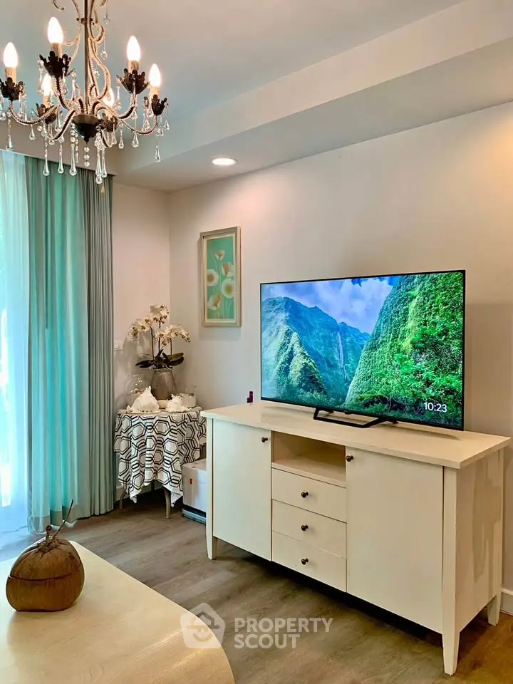Elegant living room with chandelier and modern TV setup, featuring stylish decor and natural light.