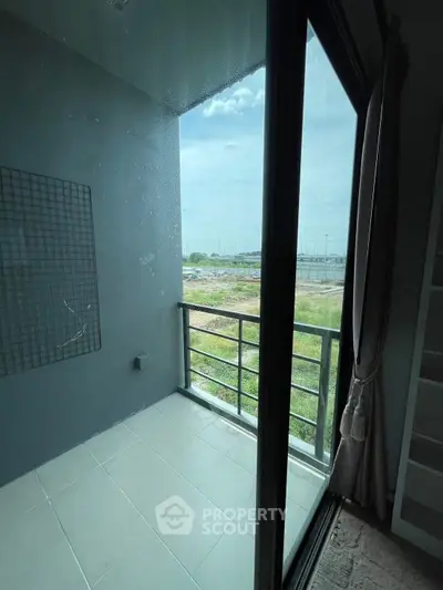 Cozy balcony with glass doors offering a serene view of open green space.