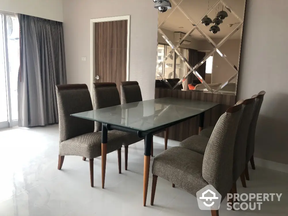 Elegant dining room with glass table and upholstered chairs, featuring mirrored wall accents.