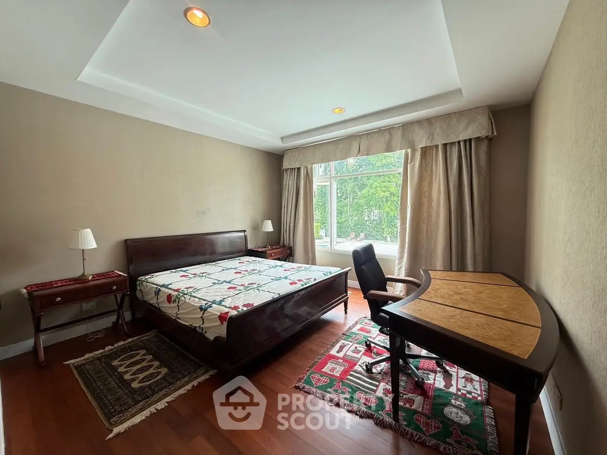 Spacious bedroom with elegant wooden furniture and large window view.