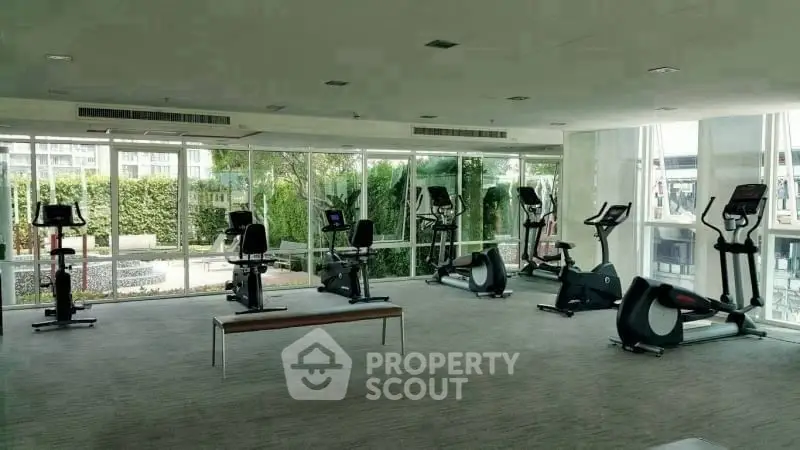 Spacious modern gym with large windows and exercise equipment in a luxury building.