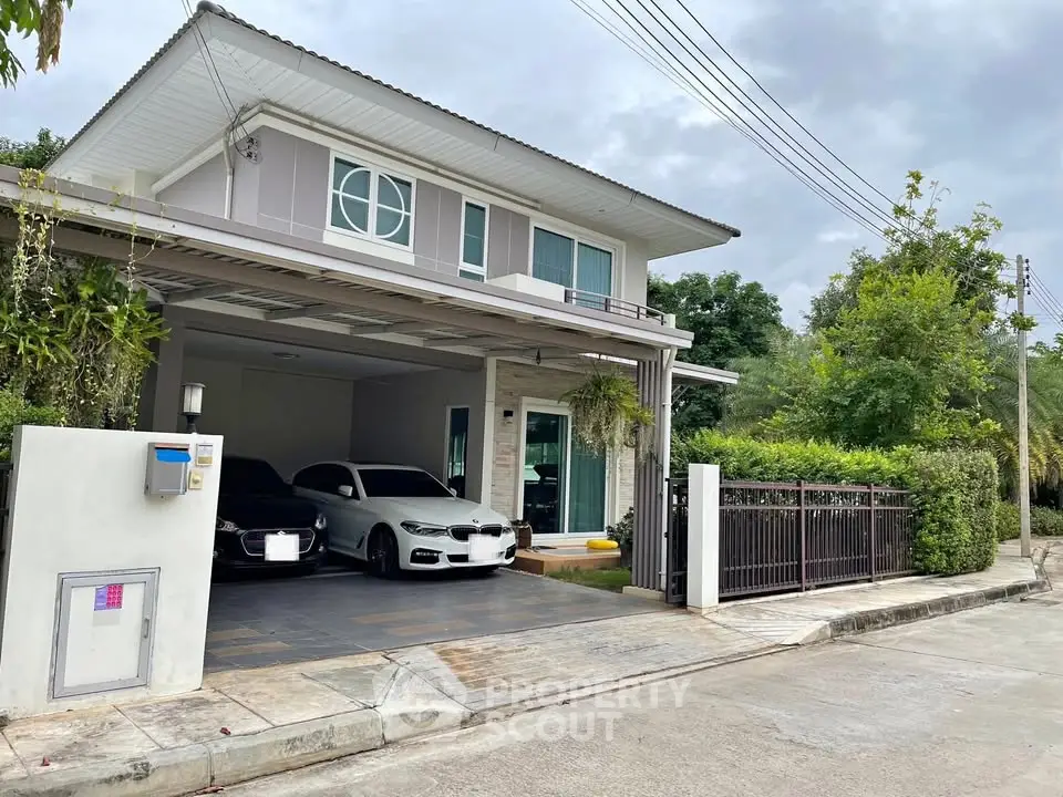 Modern two-story house with spacious driveway and two cars parked, surrounded by lush greenery.