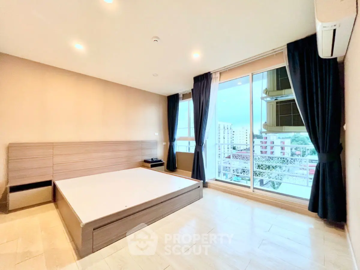 Spacious bedroom with large windows and balcony offering city views, featuring modern design and ample natural light.