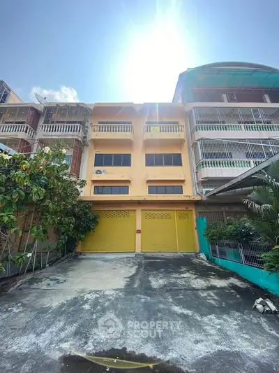 Charming multi-story townhouse with vibrant yellow garage doors and sunny facade, perfect for urban living.