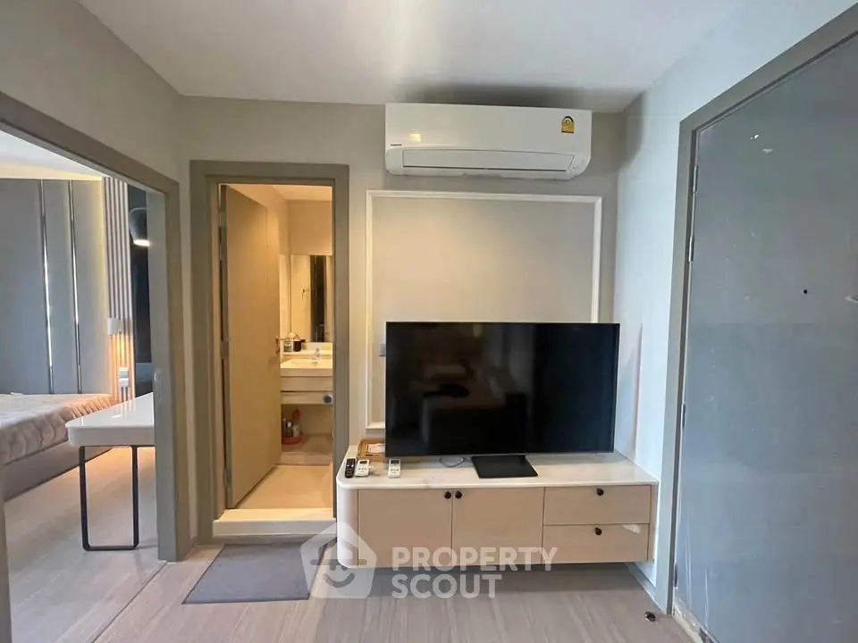 Modern living room with sleek TV setup and air conditioning, adjacent to a cozy bedroom and bathroom.