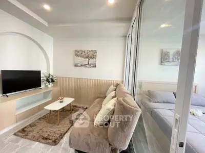 Modern living room with cozy sofa and TV, adjacent to a stylish bedroom separated by glass doors.