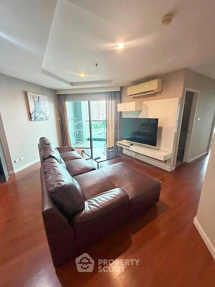 Spacious living room with modern decor and large TV, featuring a cozy leather sofa and balcony access.