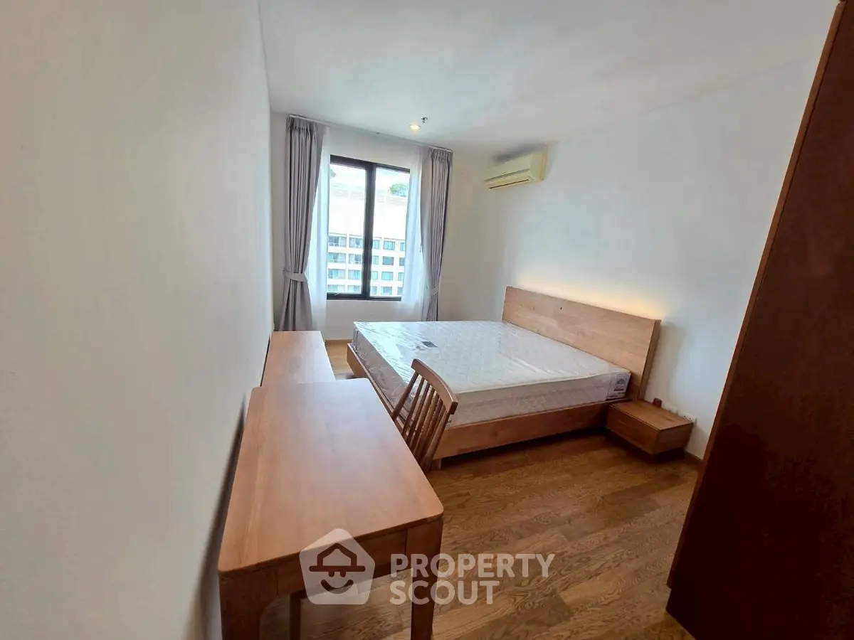 Spacious bedroom with wooden furniture and large window offering natural light.