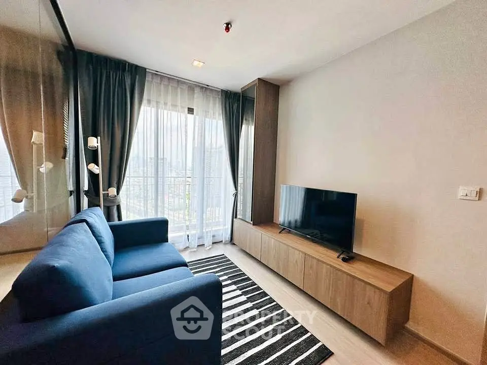 Modern living room with blue sofa, TV, and large window with sheer curtains.