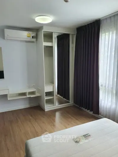 Modern bedroom with mirrored wardrobe and air conditioning, featuring elegant curtains and wooden flooring.