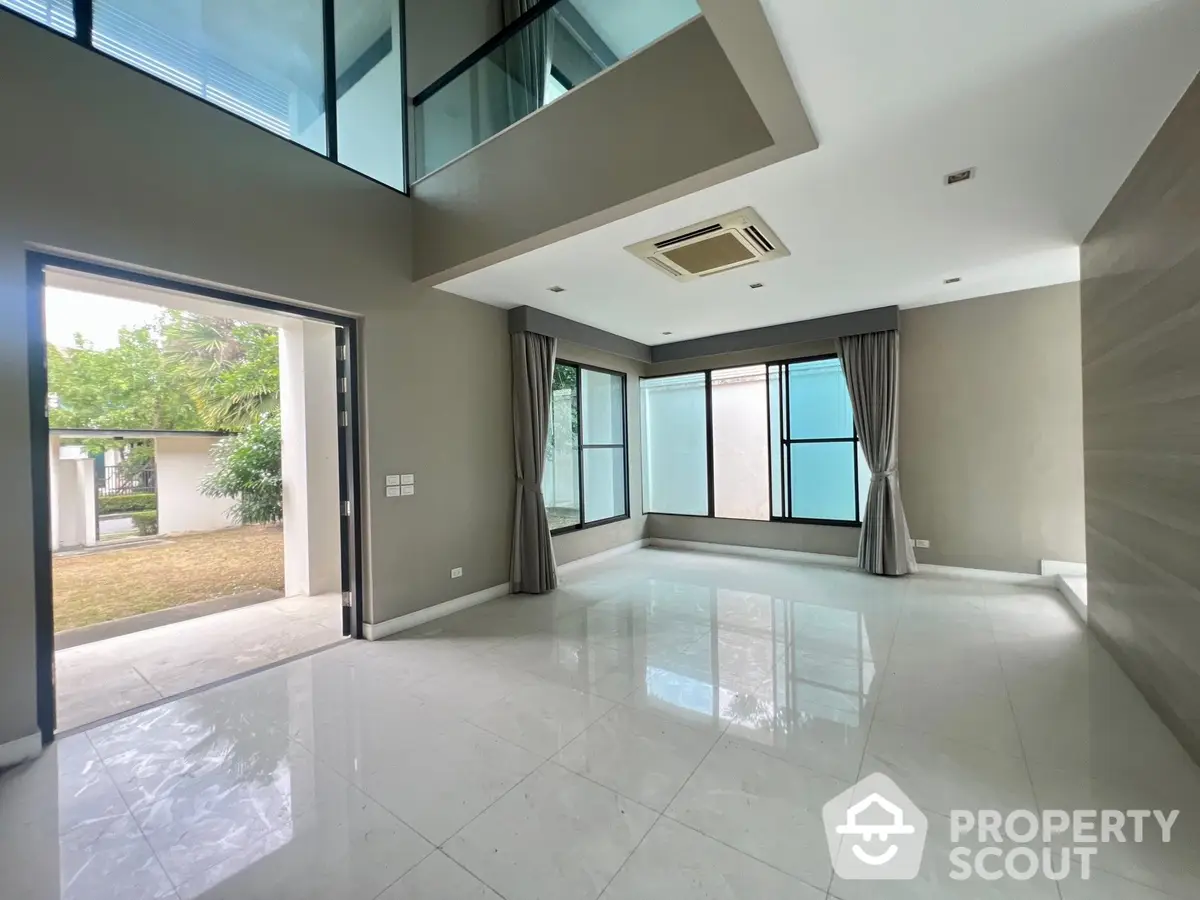 Spacious and modern living room with high ceilings, large windows, and gleaming tiled floors, opening to a serene outdoor area.