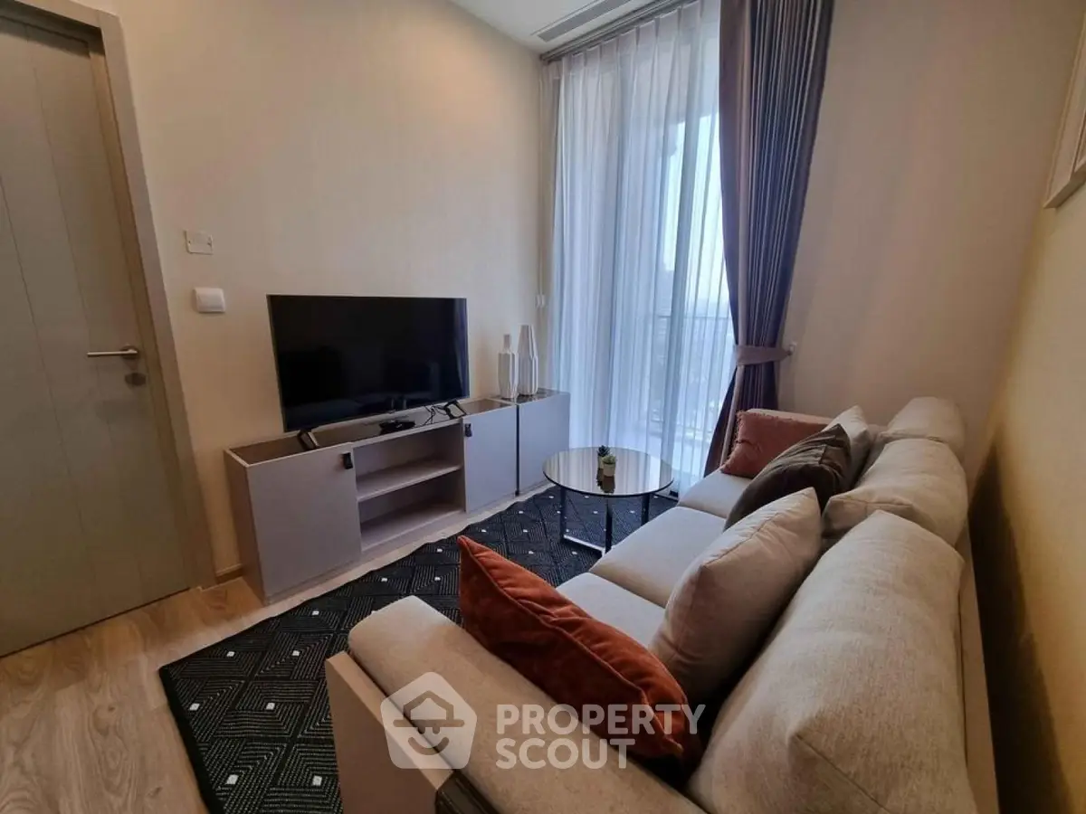 Modern living room with cozy sofa, flat-screen TV, and large window offering natural light.