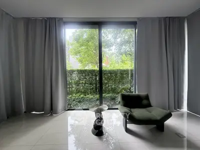 Modern living room with large window and stylish chair overlooking lush greenery.