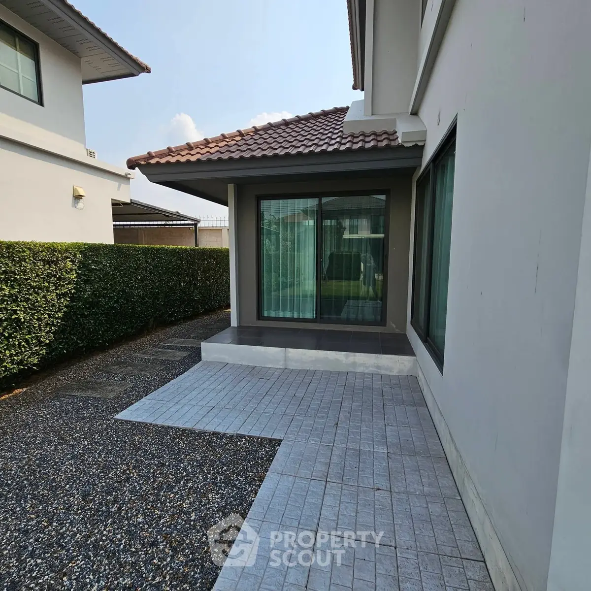 Modern house exterior with tiled patio and large windows, perfect for outdoor relaxation.