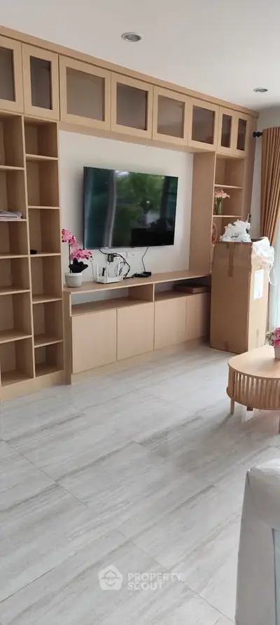 Modern living room with built-in shelves and TV, featuring elegant decor and natural light.