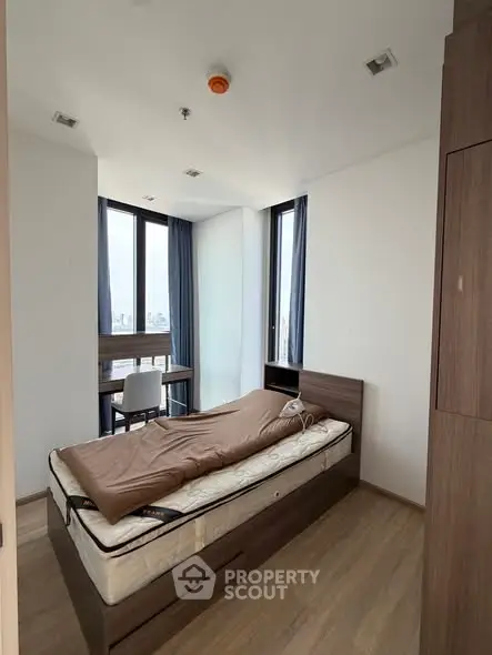 Modern bedroom with large windows and wooden flooring, featuring a single bed and study desk.