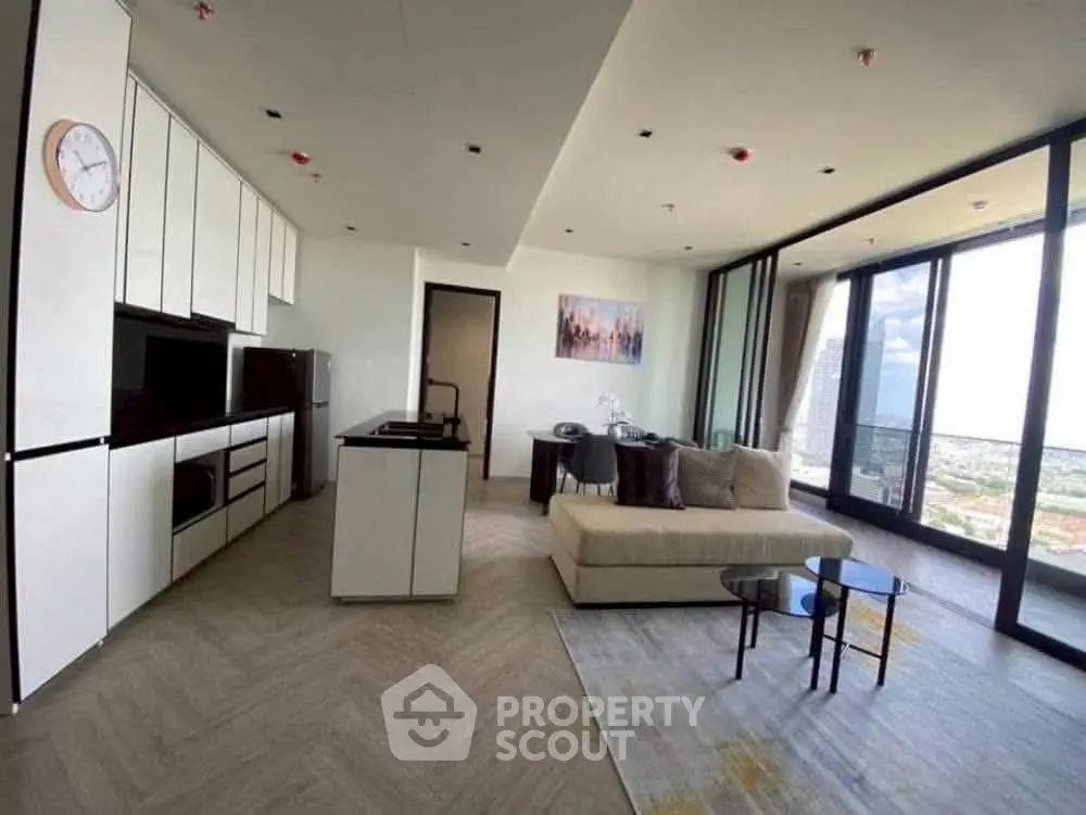 Modern open-layout living room with kitchen and city view, featuring sleek furniture and large windows.