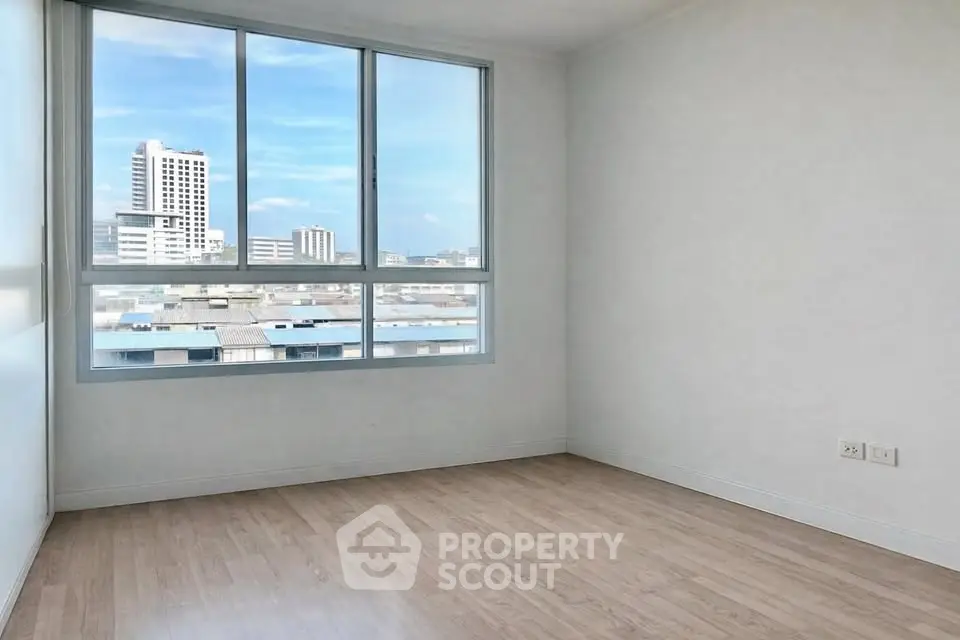 Bright empty room with large window offering city view and wooden flooring, perfect for customization.