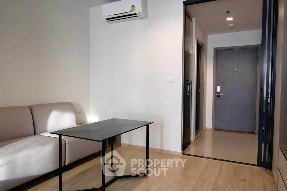 Modern living room with sleek glass table and cozy sofa, featuring a minimalist design and air conditioning.