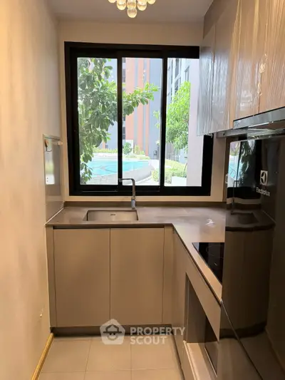 Modern kitchen with sleek cabinetry and large window overlooking greenery, featuring Electrolux appliances.