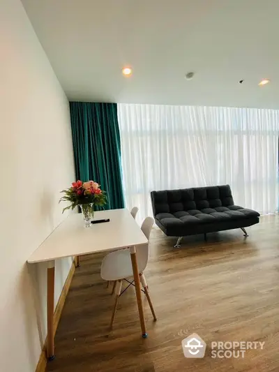 Modern living room with sleek black sofa, wooden flooring, and a stylish desk with chairs, accented by vibrant curtains.