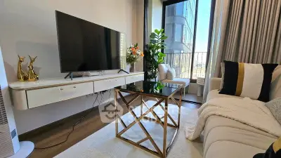 Modern living room with sleek TV, elegant decor, and balcony view in luxury apartment.