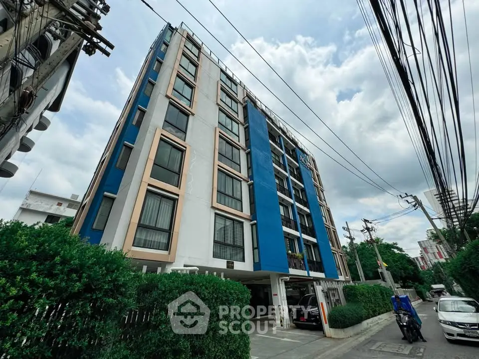 Modern urban apartment building with blue accents and lush greenery, ideal for city living.