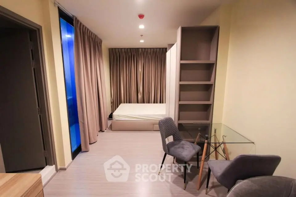 Modern bedroom with glass table and chairs, featuring a cozy bed and stylish shelving unit.