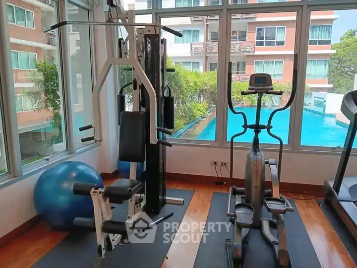 Modern gym with exercise equipment and pool view in luxury apartment complex.