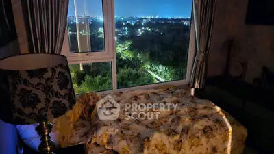 Cozy bedroom with stunning night city view through large window, elegant lamp and floral bedding.