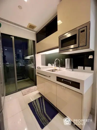 Modern kitchen with sleek cabinetry and built-in microwave, featuring a glass door leading to a balcony.