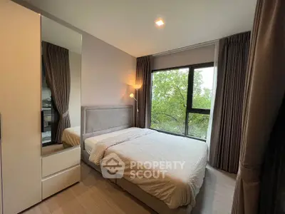Cozy bedroom with large window and modern decor, offering a serene view of lush greenery.