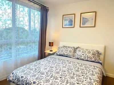 Cozy bedroom with floral bedding and large window with sheer curtains, perfect for relaxation.