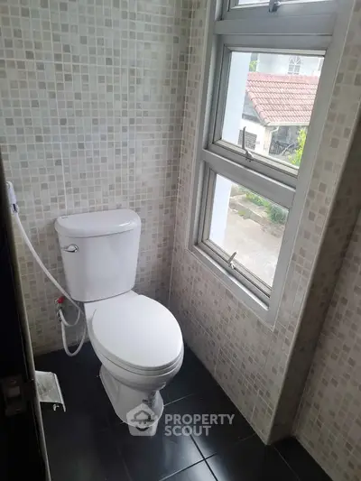 Compact bathroom with modern toilet and tiled walls, featuring a window with a view.