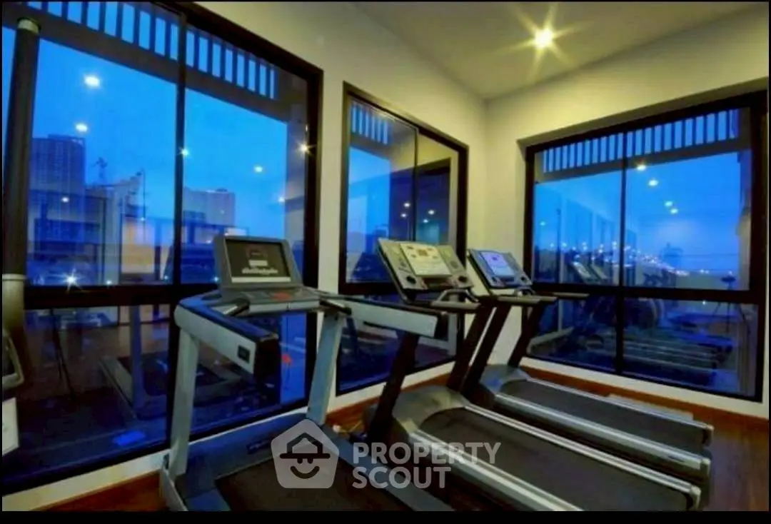 Modern gym with city view featuring treadmills and large windows for natural light.