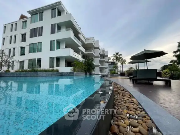 Luxurious modern apartment building with stunning poolside view and elegant outdoor seating area.
