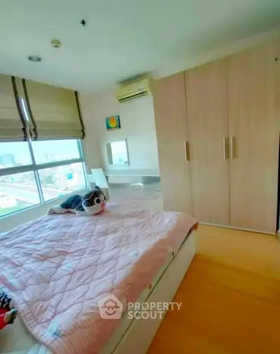 Cozy bedroom with large window and city view, featuring modern wardrobe and air conditioning.