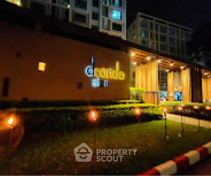 Modern building entrance with illuminated signage and landscaped garden at night.