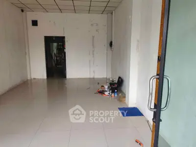 Spacious empty commercial space with tiled flooring and glass door entrance.