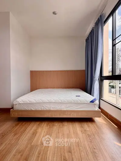Modern bedroom with large window and wooden flooring, featuring a minimalist bed and stylish headboard.